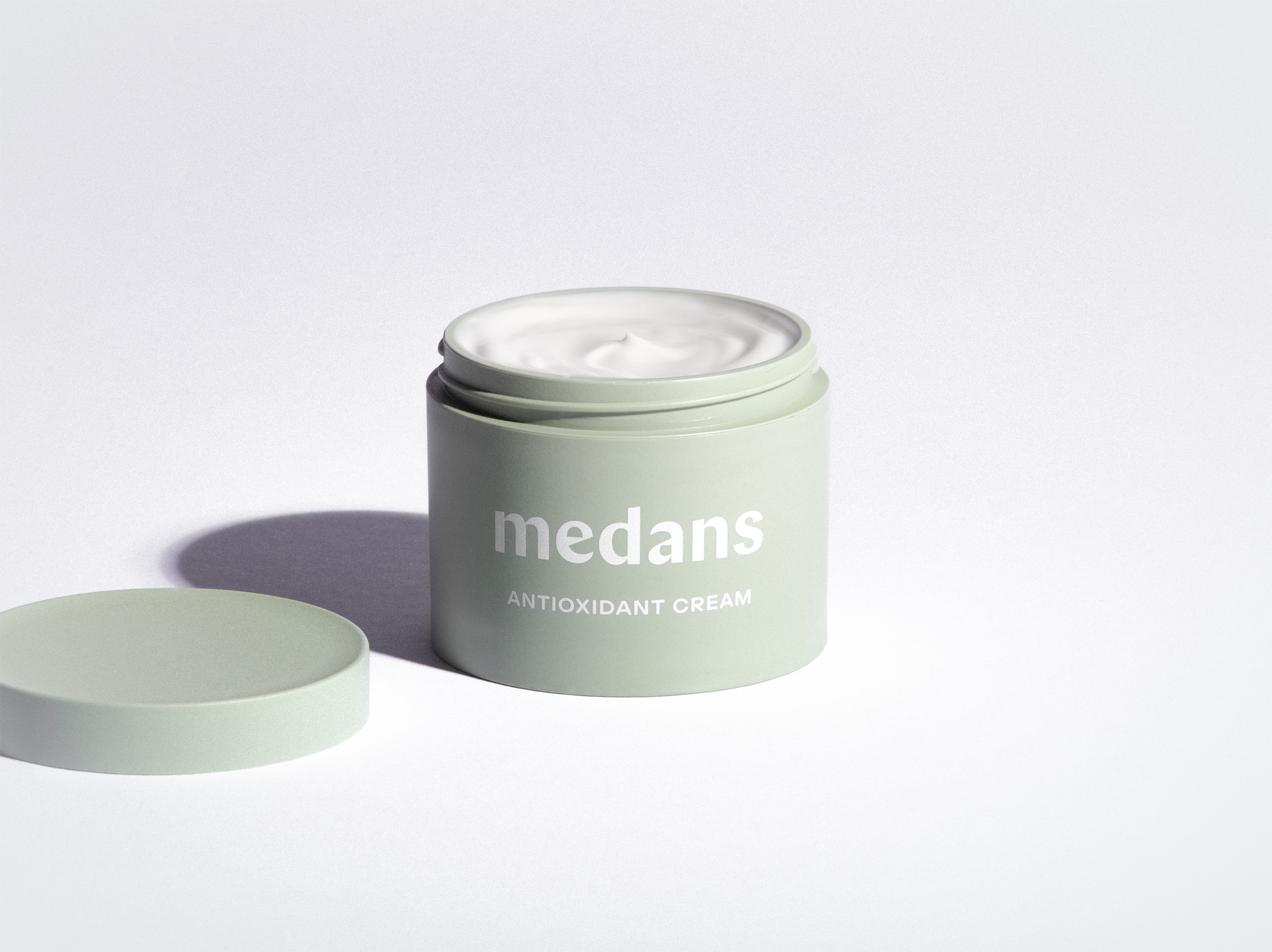 Green jar of medans antioxidant cream on a light gray background