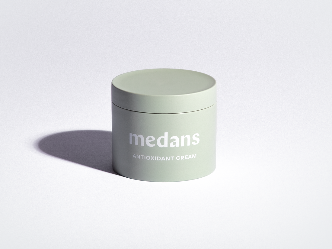 Green jar of medans antioxidant cream on a light gray background