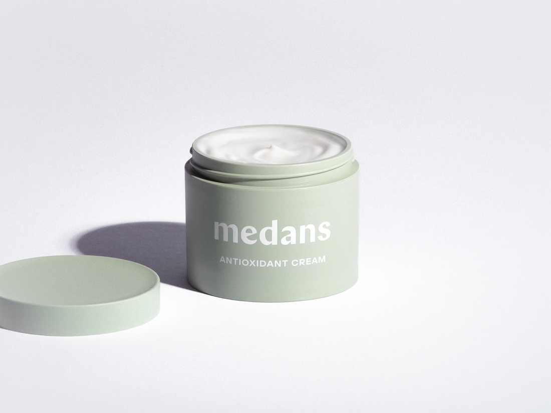 Green jar of medans antioxidant cream on a light gray background