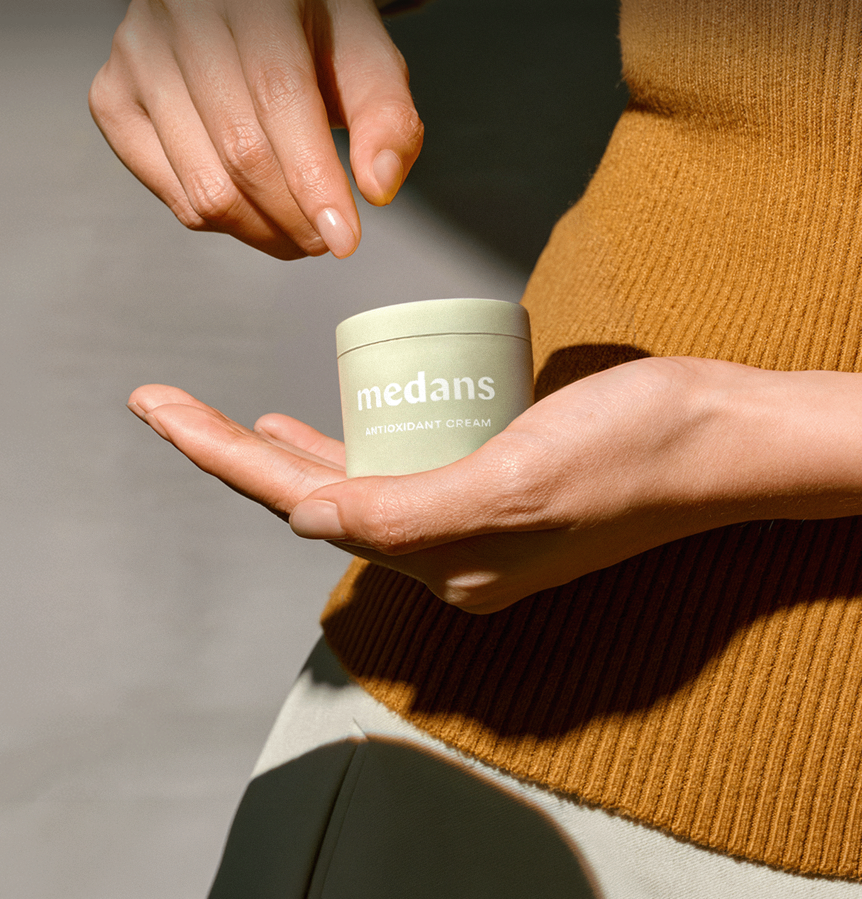 Person holding a container of Medans cream in their palm.